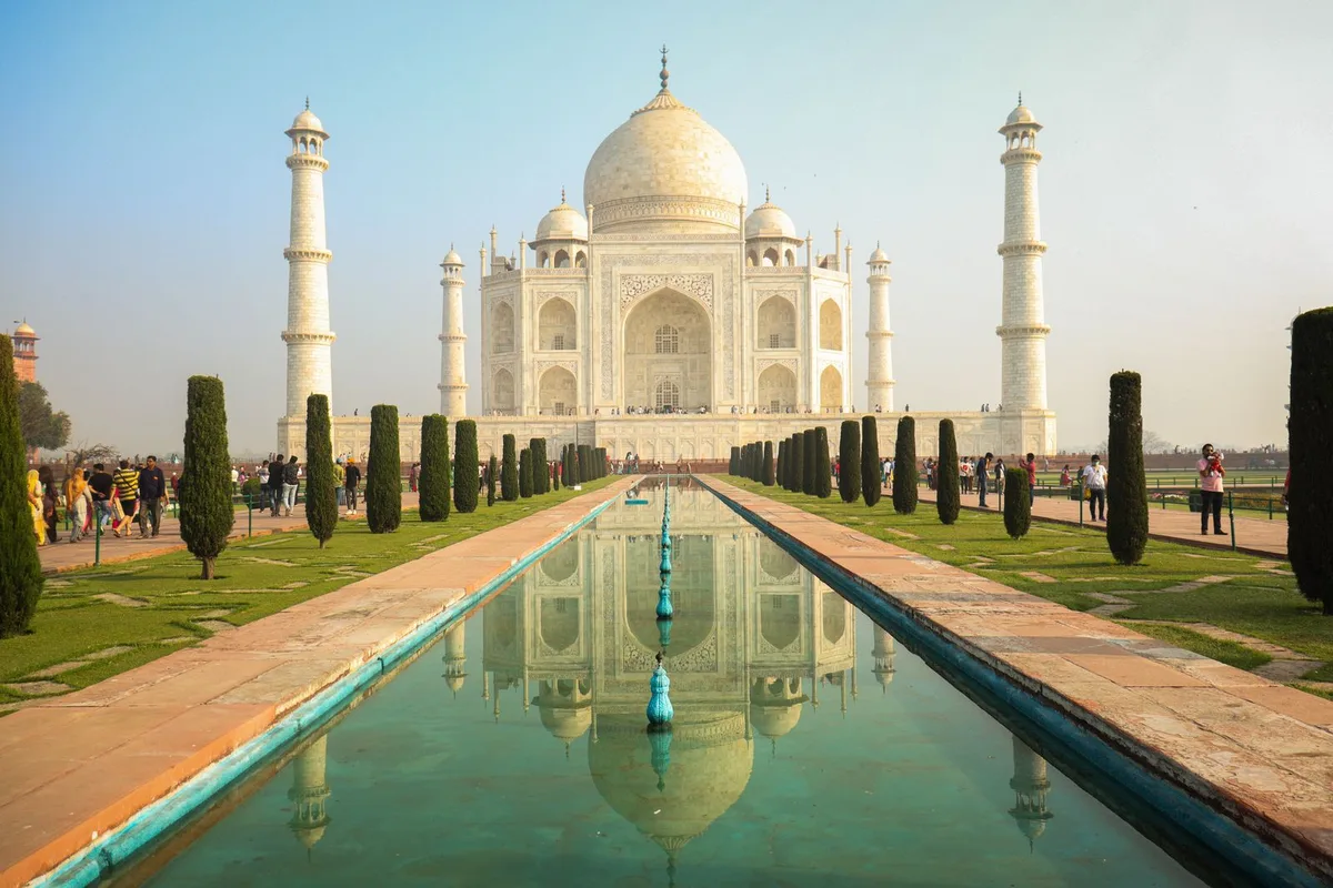 The Taj Mahal from the charbagh gardens, reflected in the long central pool under a blue sky