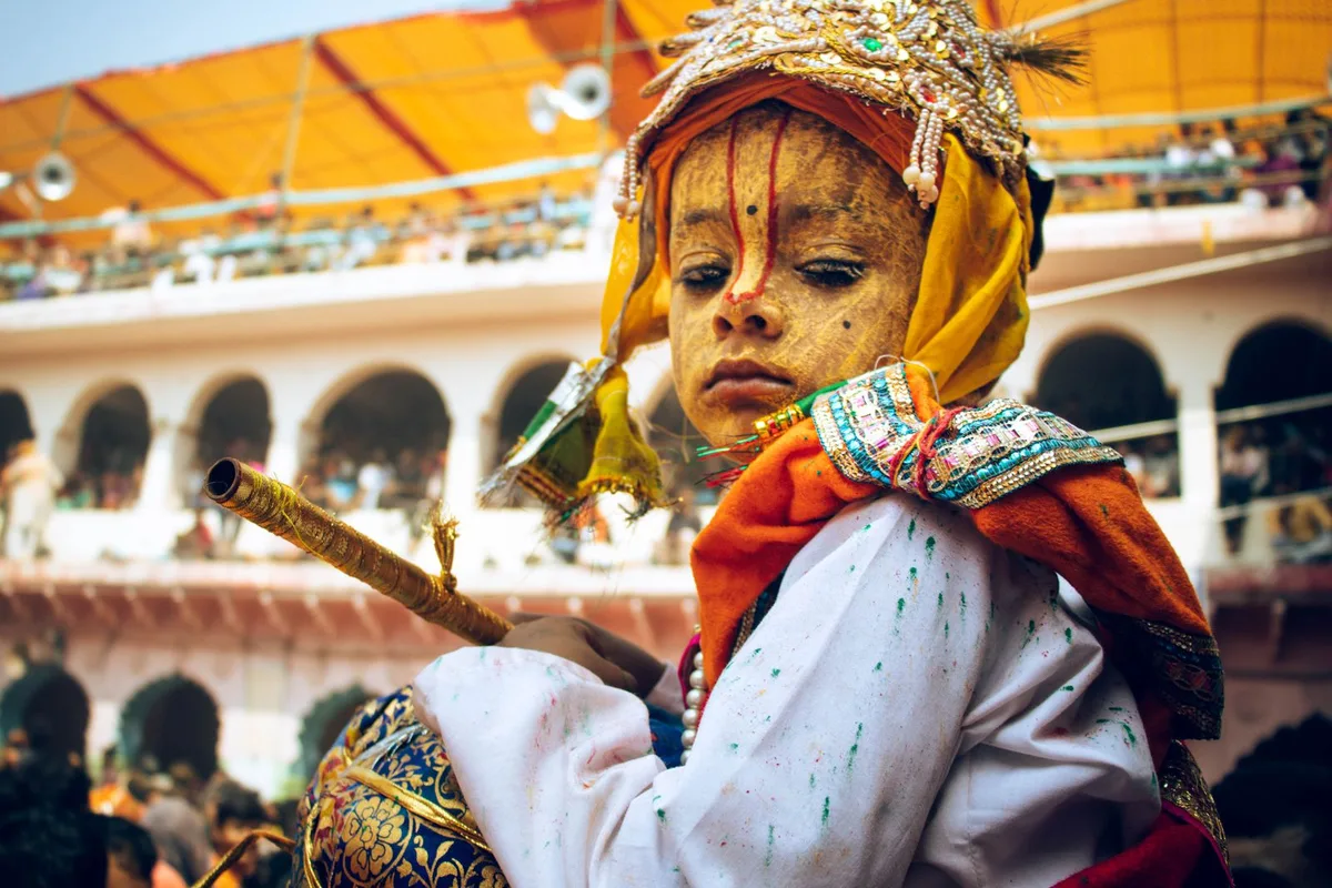 A child dressed as Krishna, flute in hand, at a temple festival in Vrindavan