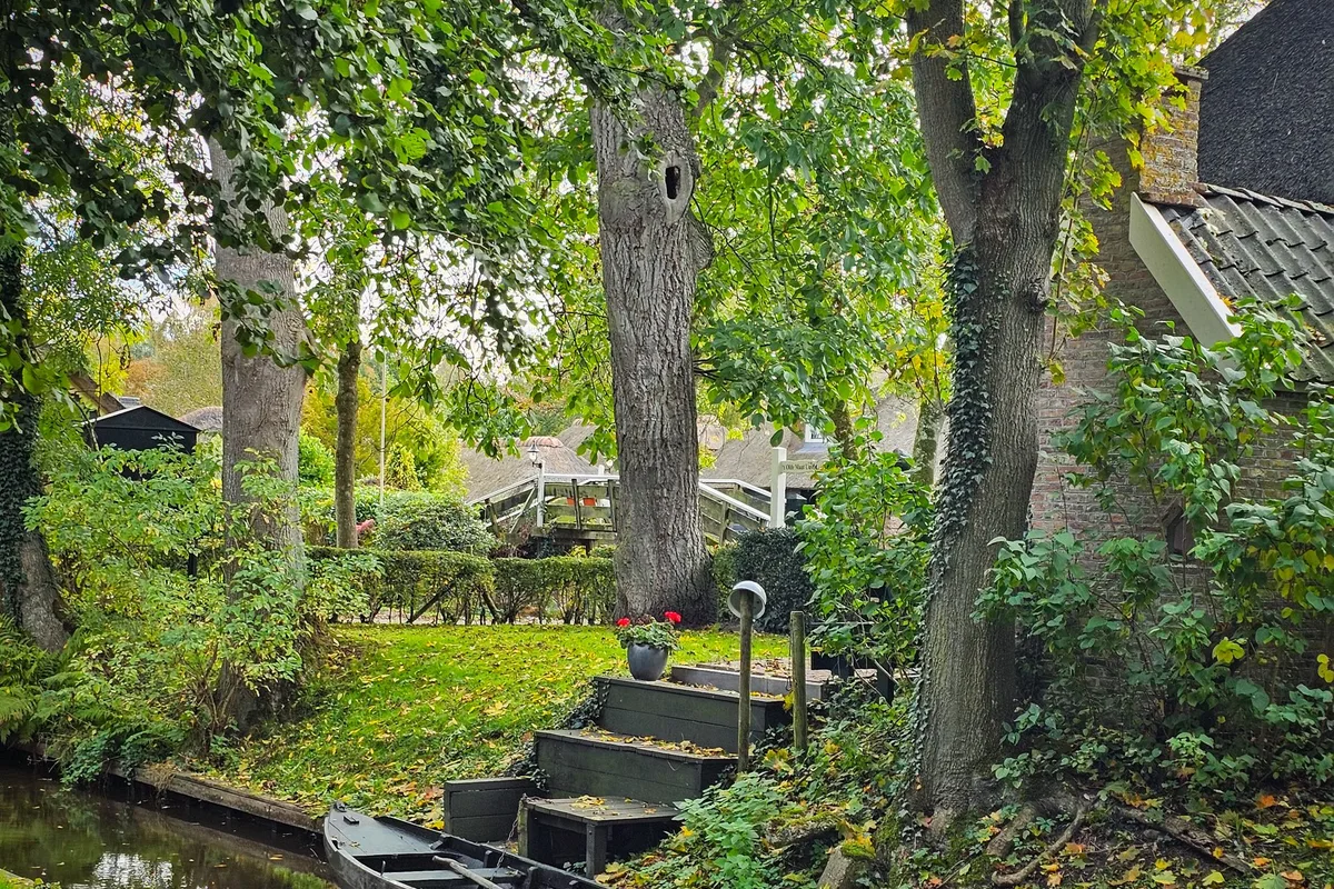 A boat moored on a green, tree-lined canal in Giethoorn