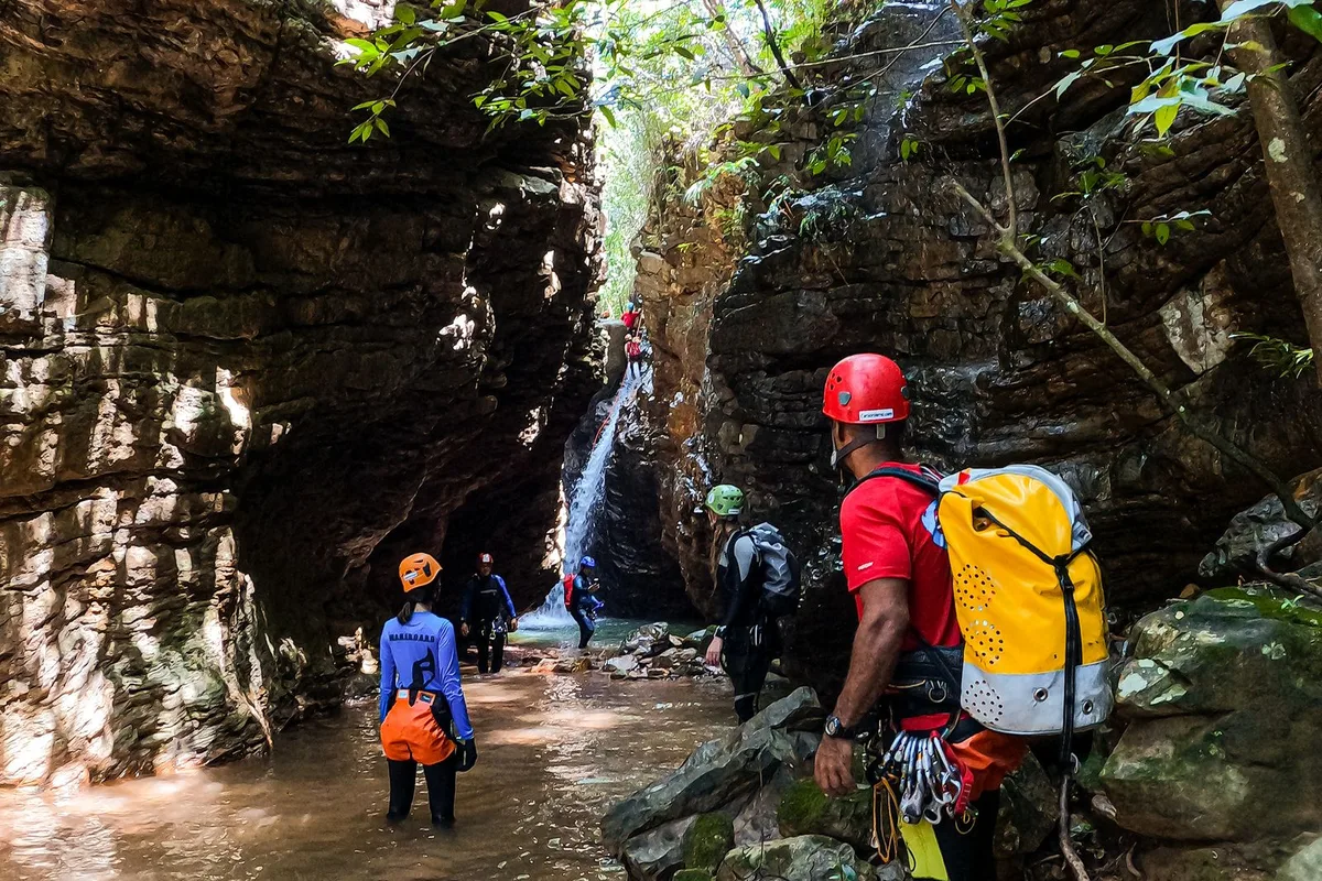 A guided canyoning group in helmets and wetsuits wading through a narrow rock gorge