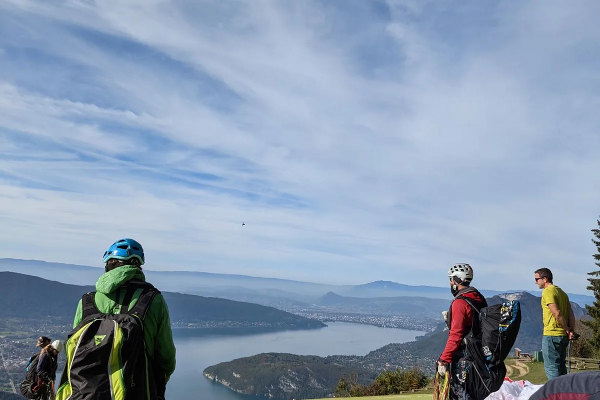 Paragliders preparing to launch from a grassy col above a mountain lake