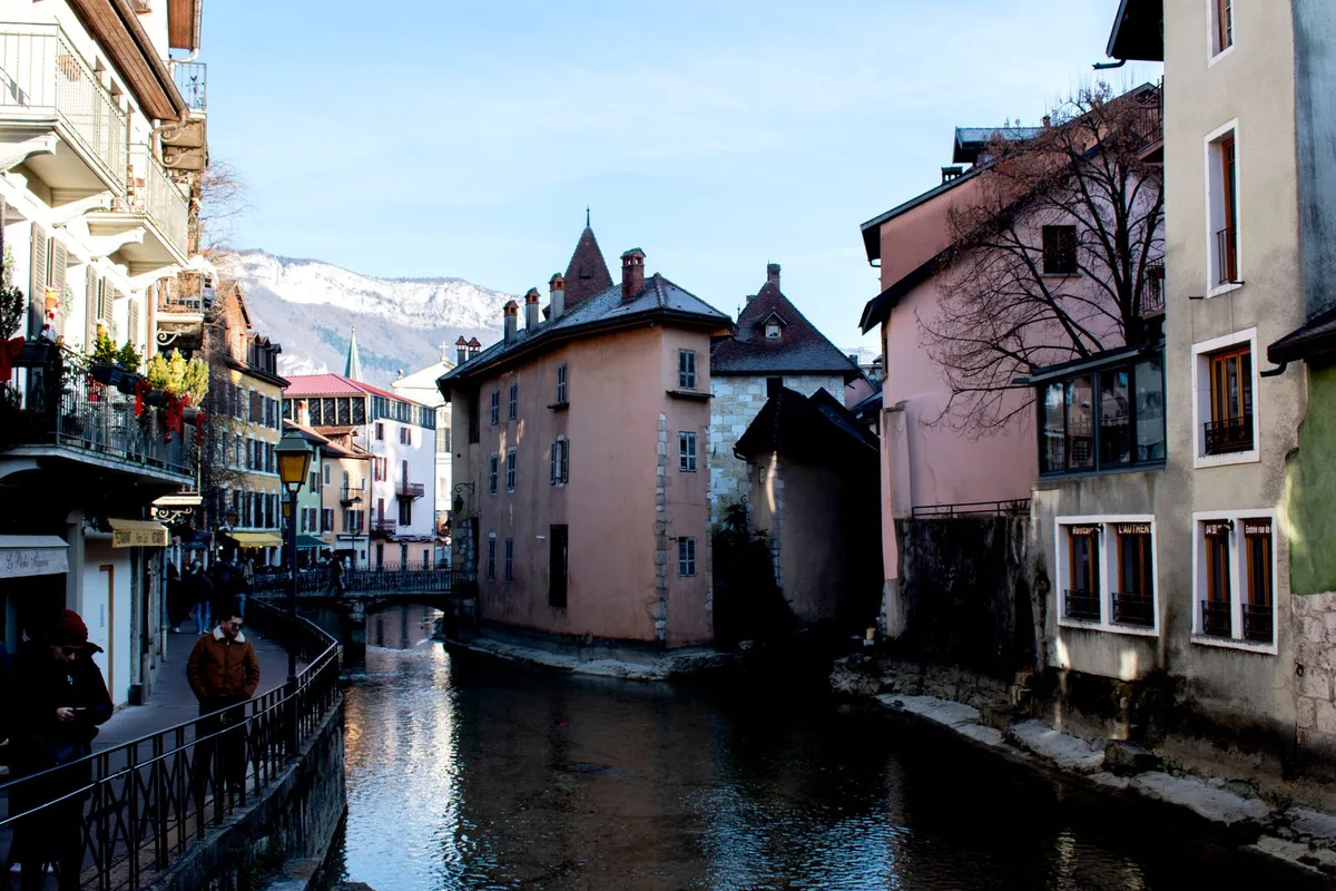 An Annecy old town canal in winter, with snow on the mountains behind the rooftops