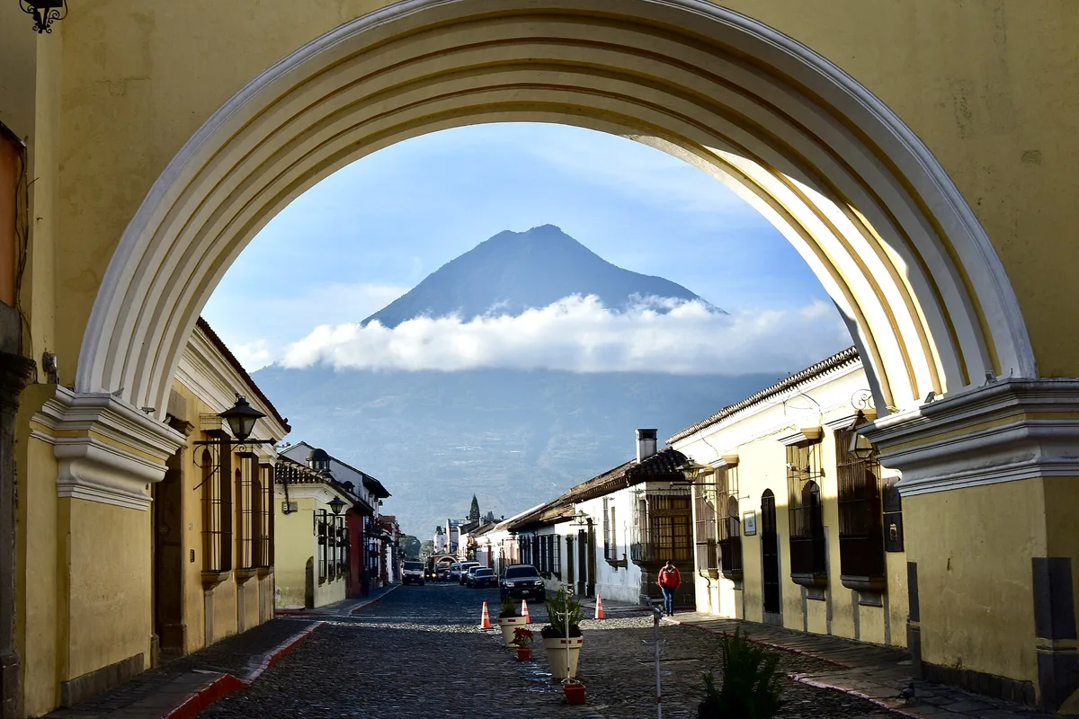 A cobbled Antigua street framed by an arch, with a volcano beyond