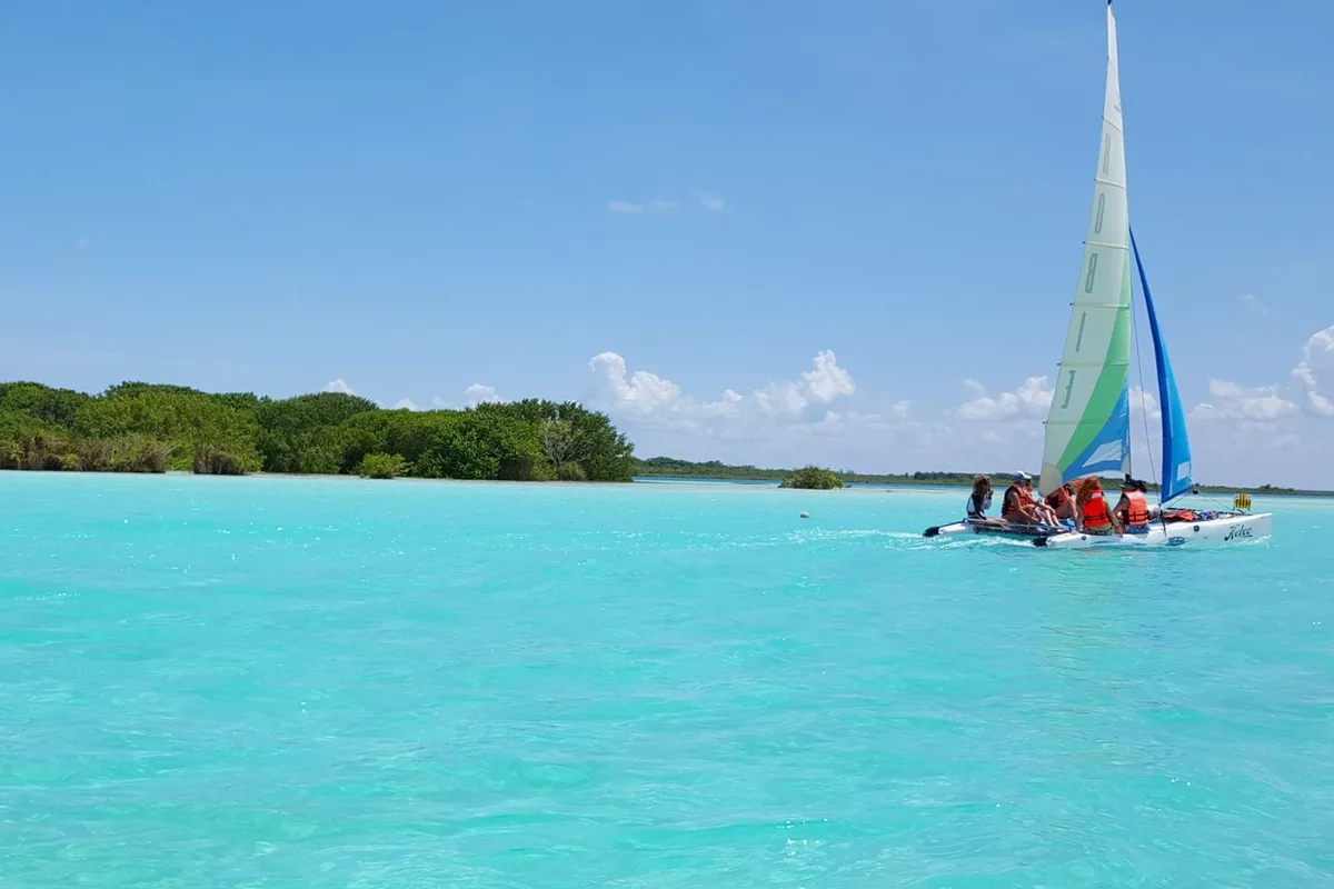 A catamaran under a bright sail on the turquoise lagoon