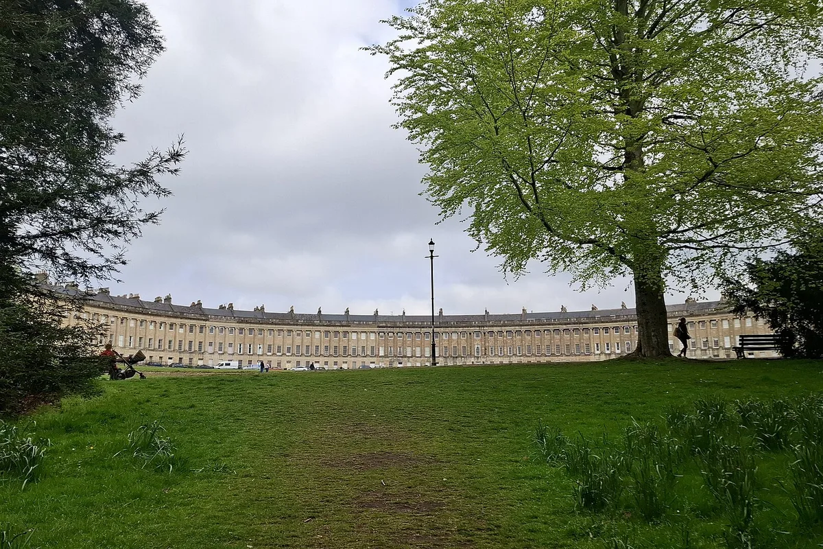 The Royal Crescent sweeping across its lawn in Bath, honey-coloured stone under a cloudy sky