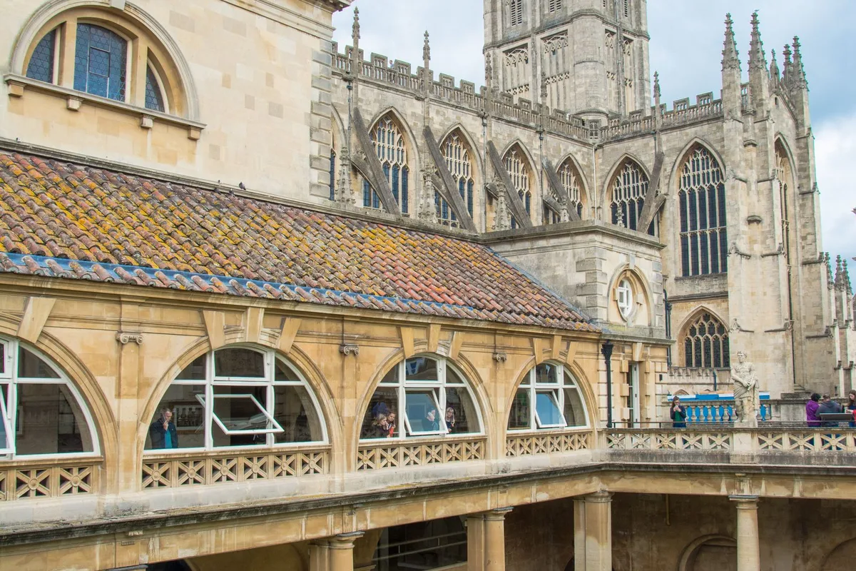 The Great Bath at the Roman Baths, green spring water below the colonnade with Bath Abbey behind
