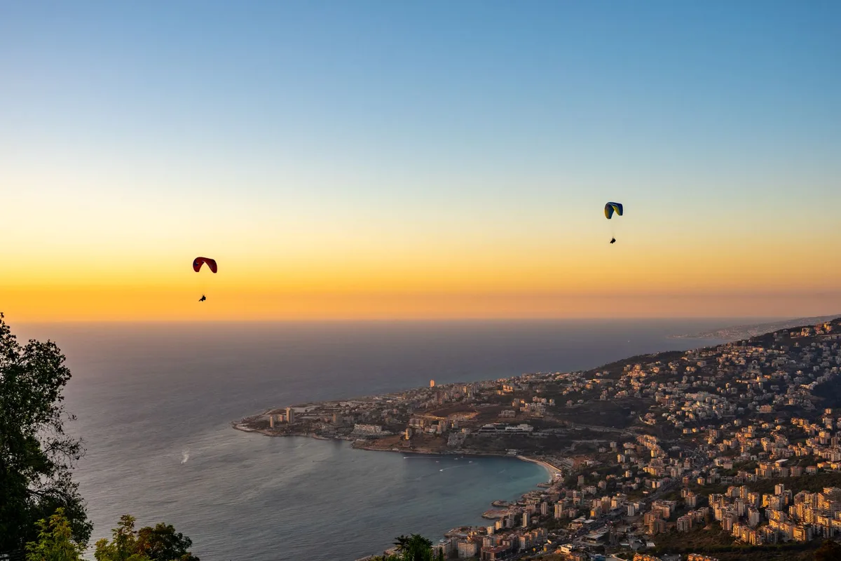 Jounieh Bay at sunset from the Harissa hillside, paragliders overhead