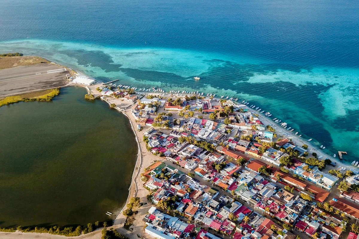 San Pedro Town from the air — airstrip and lagoon behind the rooftops, the reef out front