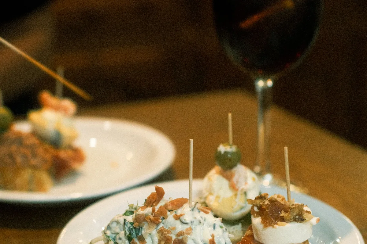 Pintxos lined up on a Bilbao bar counter, skewered bites on bread beside a glass of red wine