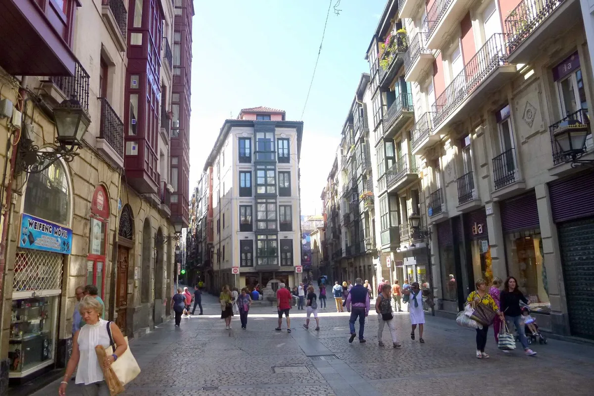 A pedestrian street in Bilbao's Casco Viejo, lined with balconied apartment buildings and small shops