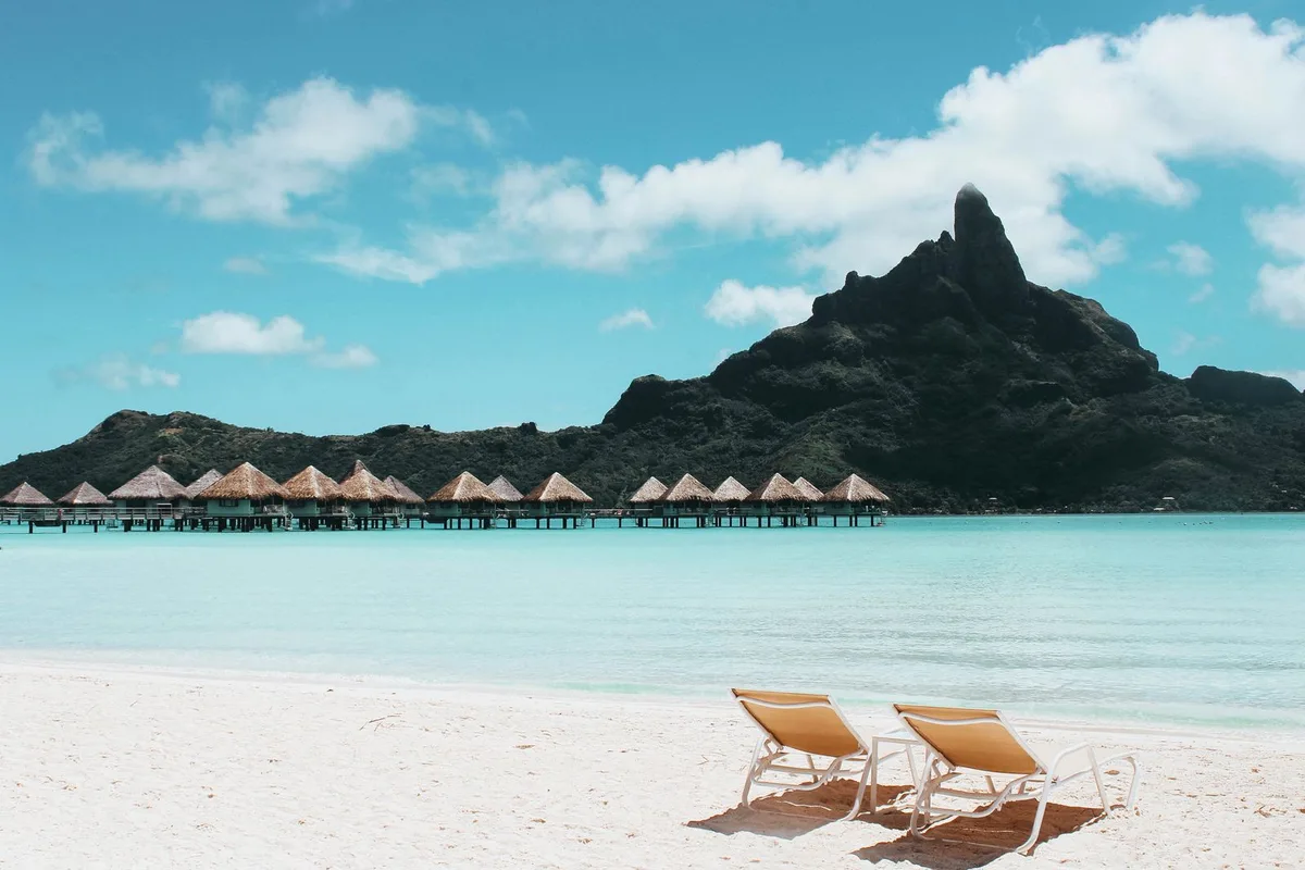 Matira Beach at Bora Bora — loungers on white sand, overwater bungalows and Mount Otemanu behind
