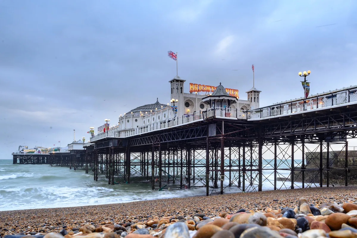 Brighton Palace Pier from the pebble beach, its white pavilion and fairground rides over the sea