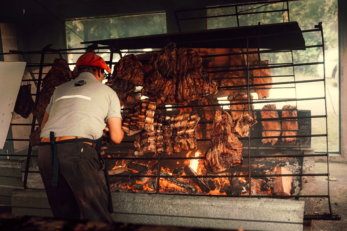 Beef grilling over an open wood fire, tended by the parrillero