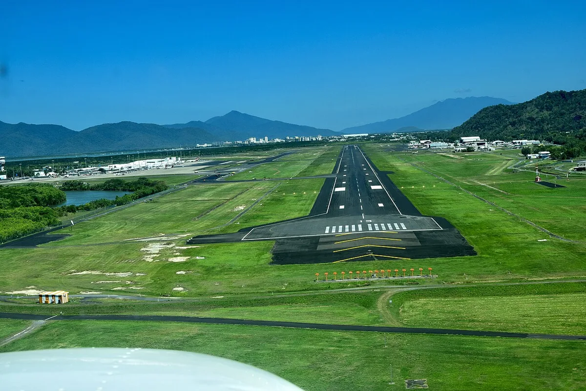 Cairns Airport's runway from the air on final approach, green fields and the ranges behind