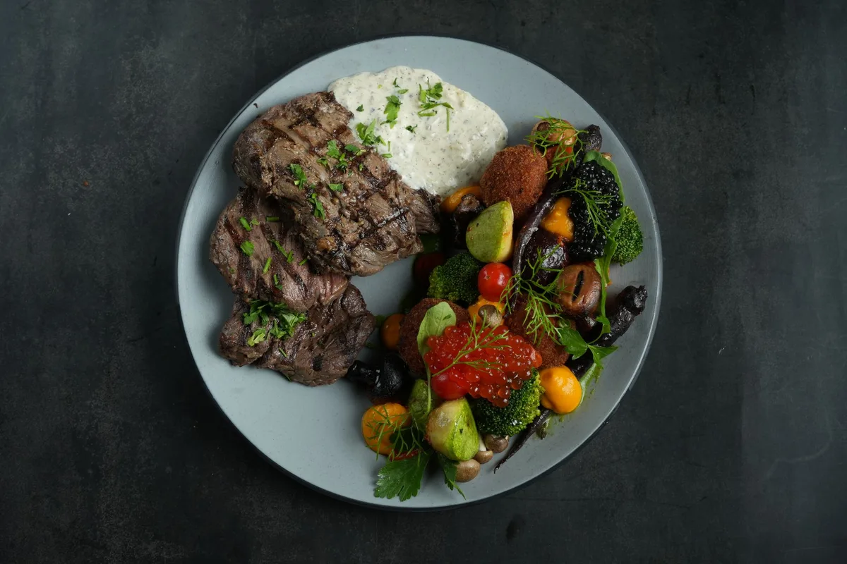 A grilled Alberta steak with roast vegetables and mash on a dark slate table