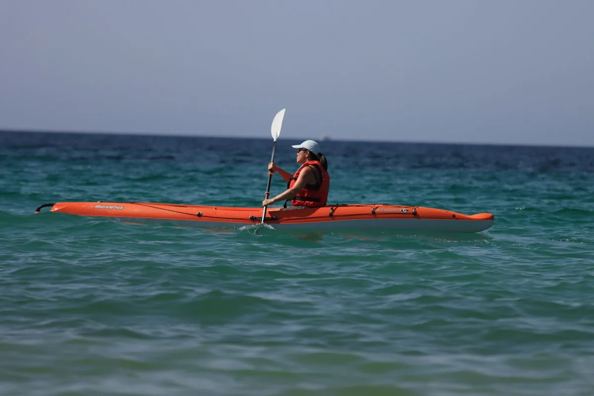 A kayaker paddling an orange sea kayak on open blue water
