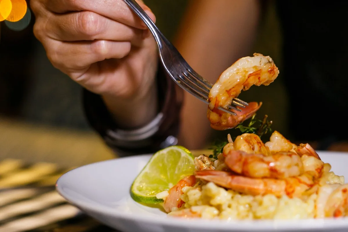 A fork lifting a shrimp over a bowl of shrimp and grits
