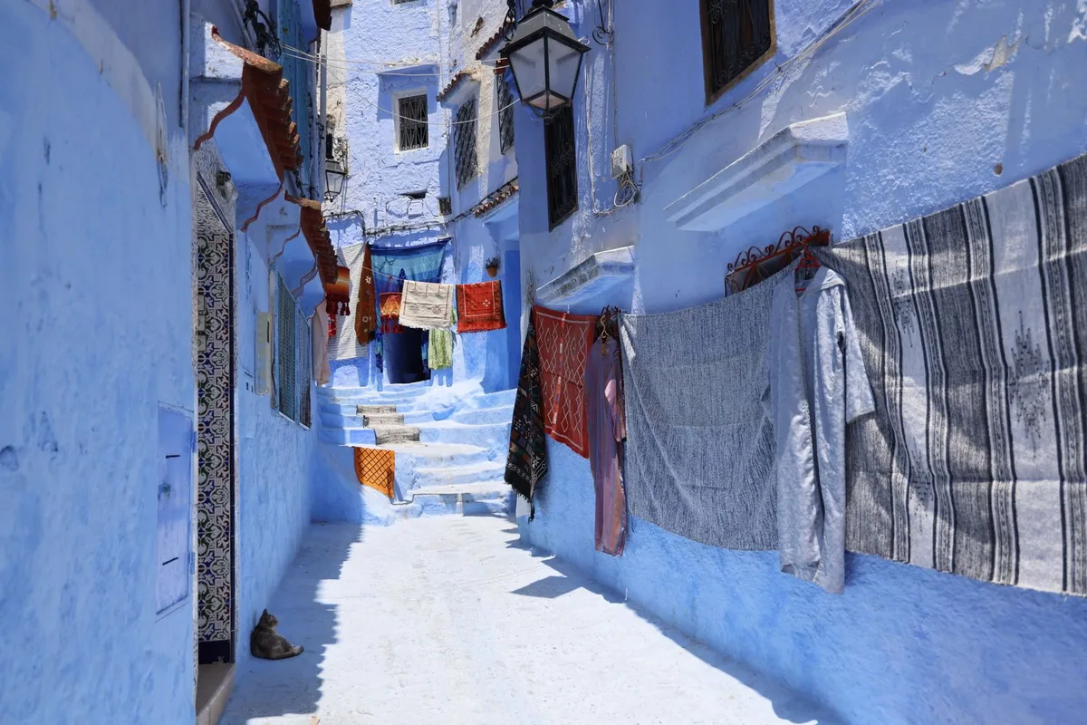 Woven textiles hanging in a blue Chefchaouen medina lane