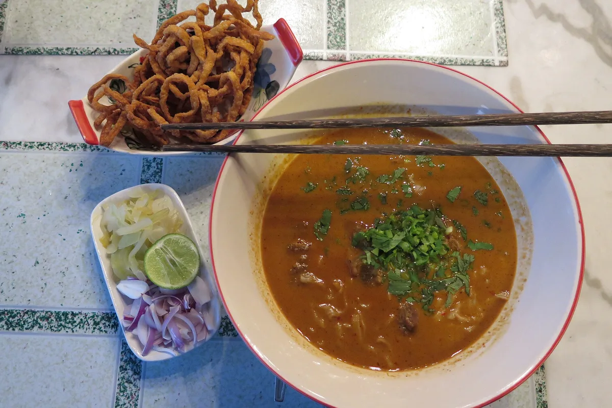 A bowl of khao soi with crispy noodles, pickled greens, lime and shallots alongside