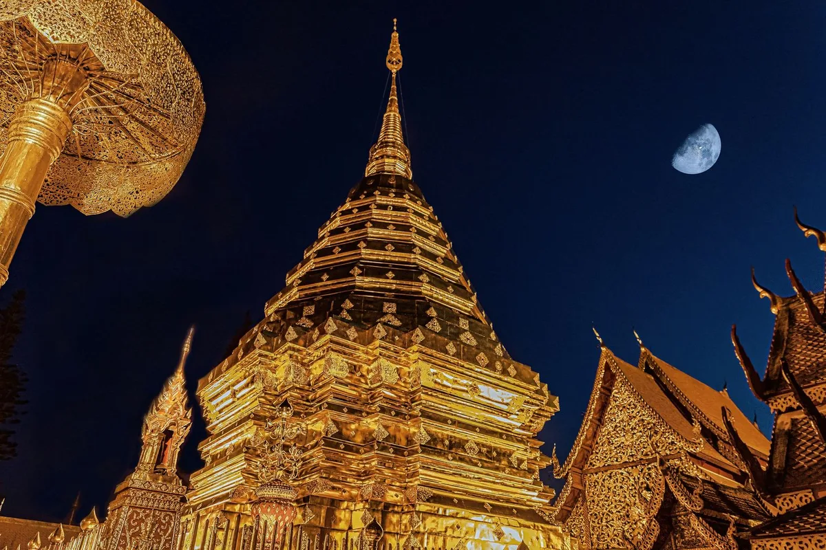 A golden Lanna chedi glowing at dusk under a crescent moon in Chiang Mai