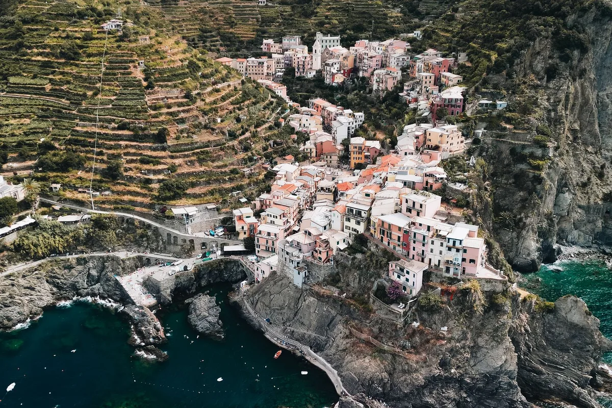 A Cinque Terre village on its rocky point from the air, a boat crossing the bay below