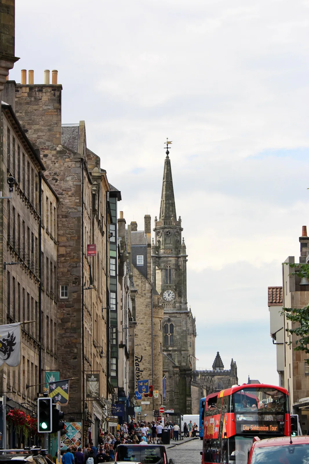 The Royal Mile looking up to the Tron Kirk tower, crowded, with a red sightseeing bus
