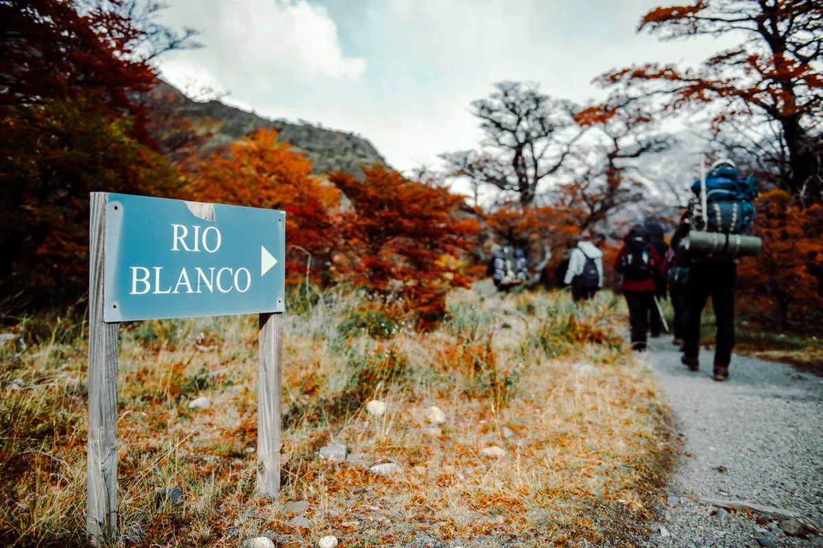 Hikers passing the Río Blanco trail sign under autumn lenga trees near El Chaltén