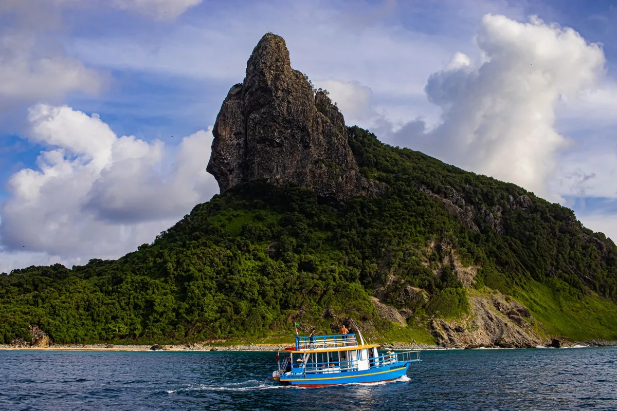 A tour boat on blue water below Morro do Pico