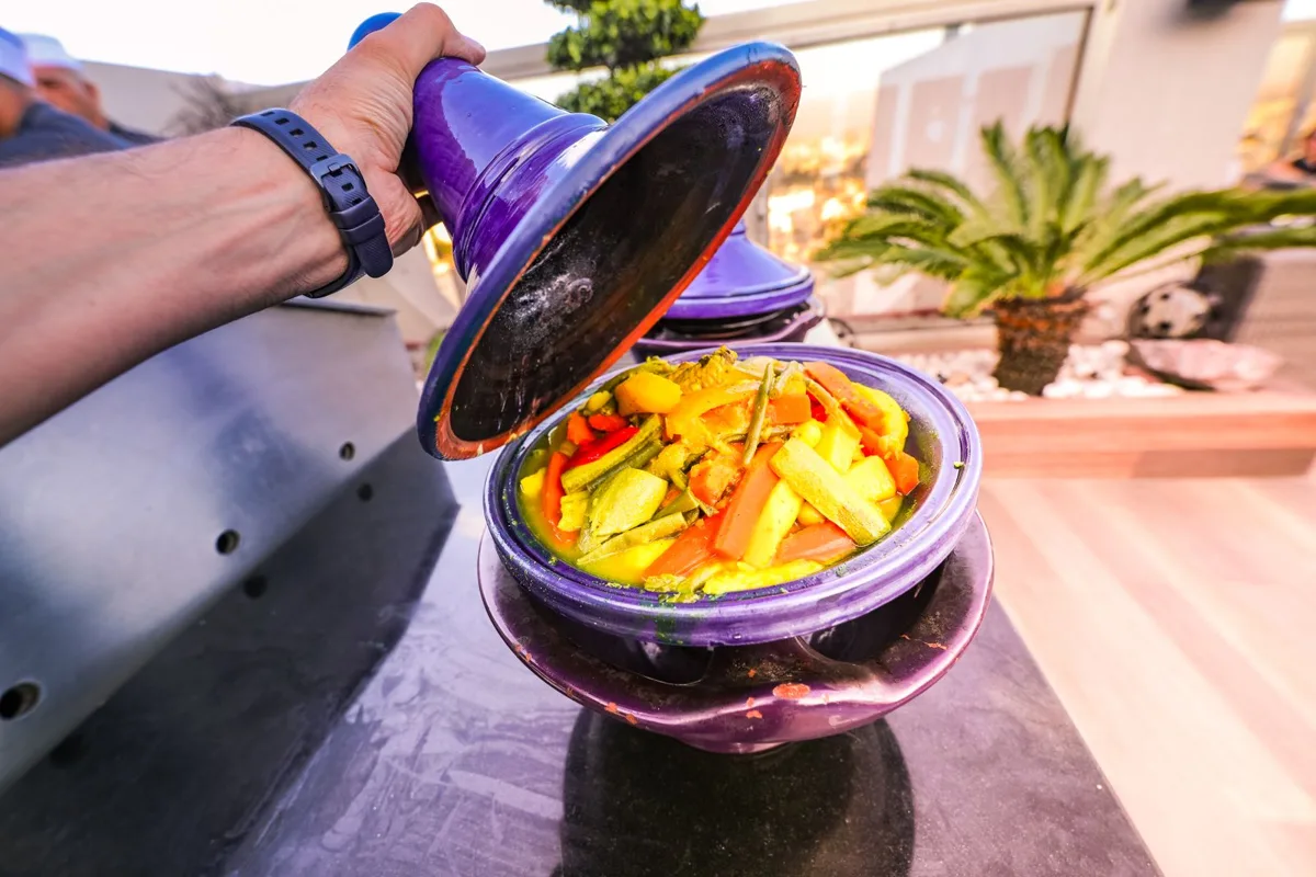 A vegetable tagine being opened at a rooftop table