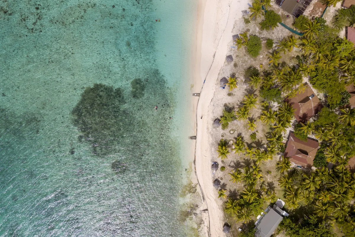 A Fiji island beach from above — palms, white sand and the reef edge in stacked turquoise