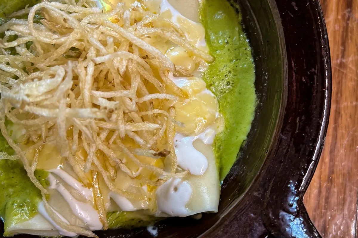 An enchilada in green sauce with cheese and onion, served in a clay dish