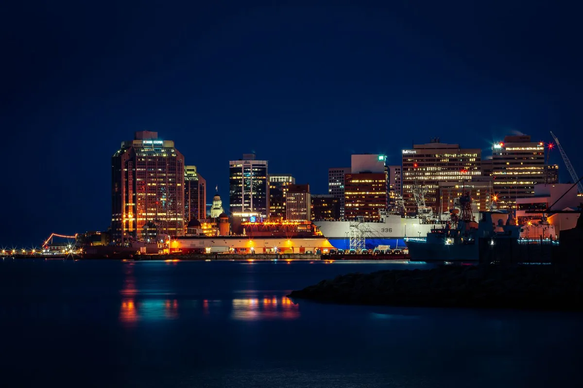 Downtown Halifax lit up across the harbour at night, the towers reflected in the water