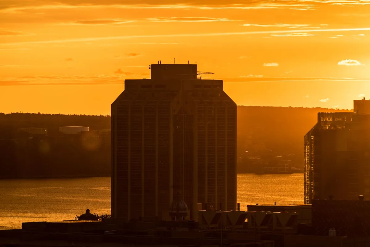 A downtown Halifax tower silhouetted against an orange harbour sunset