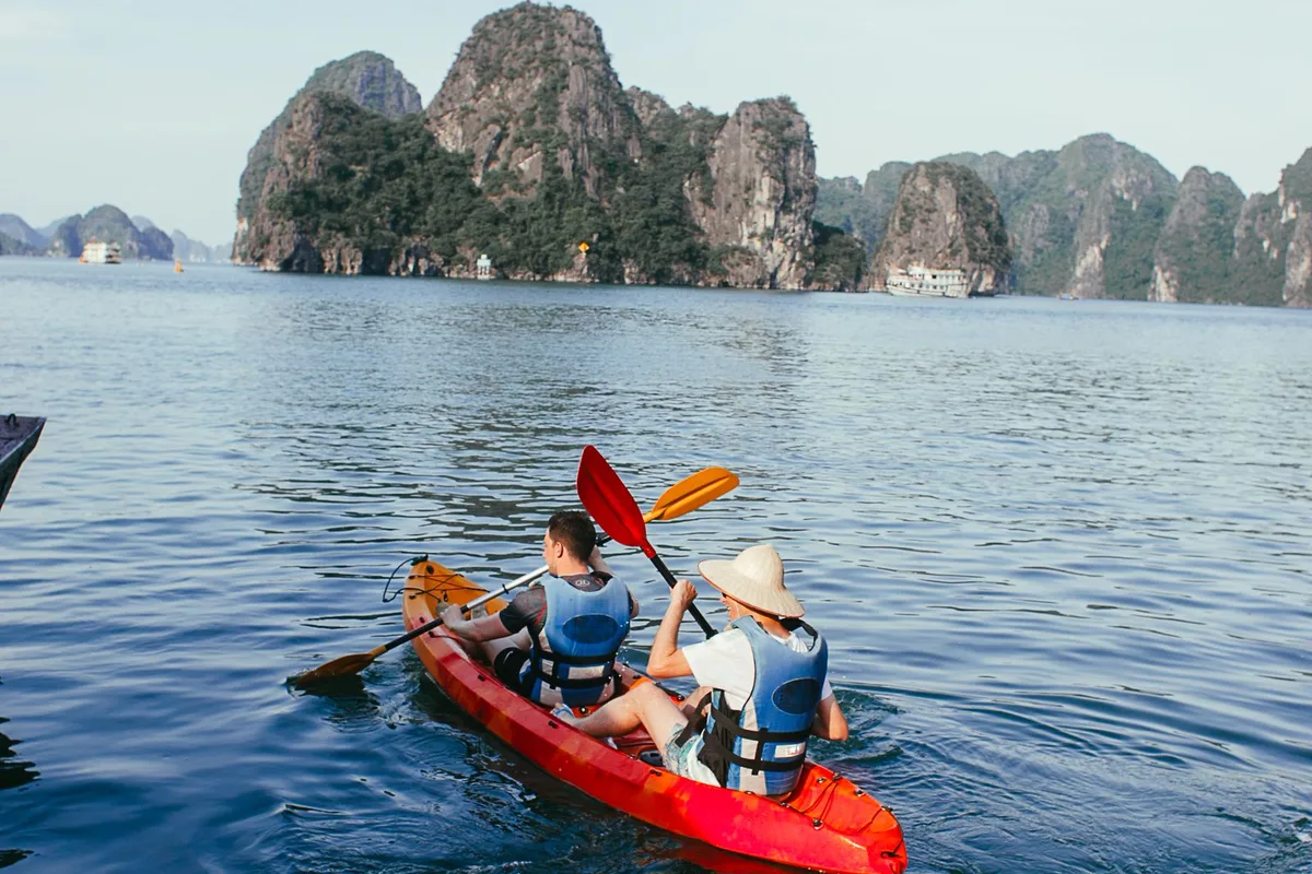 Two kayakers paddling a red kayak toward the karsts of Ha Long Bay