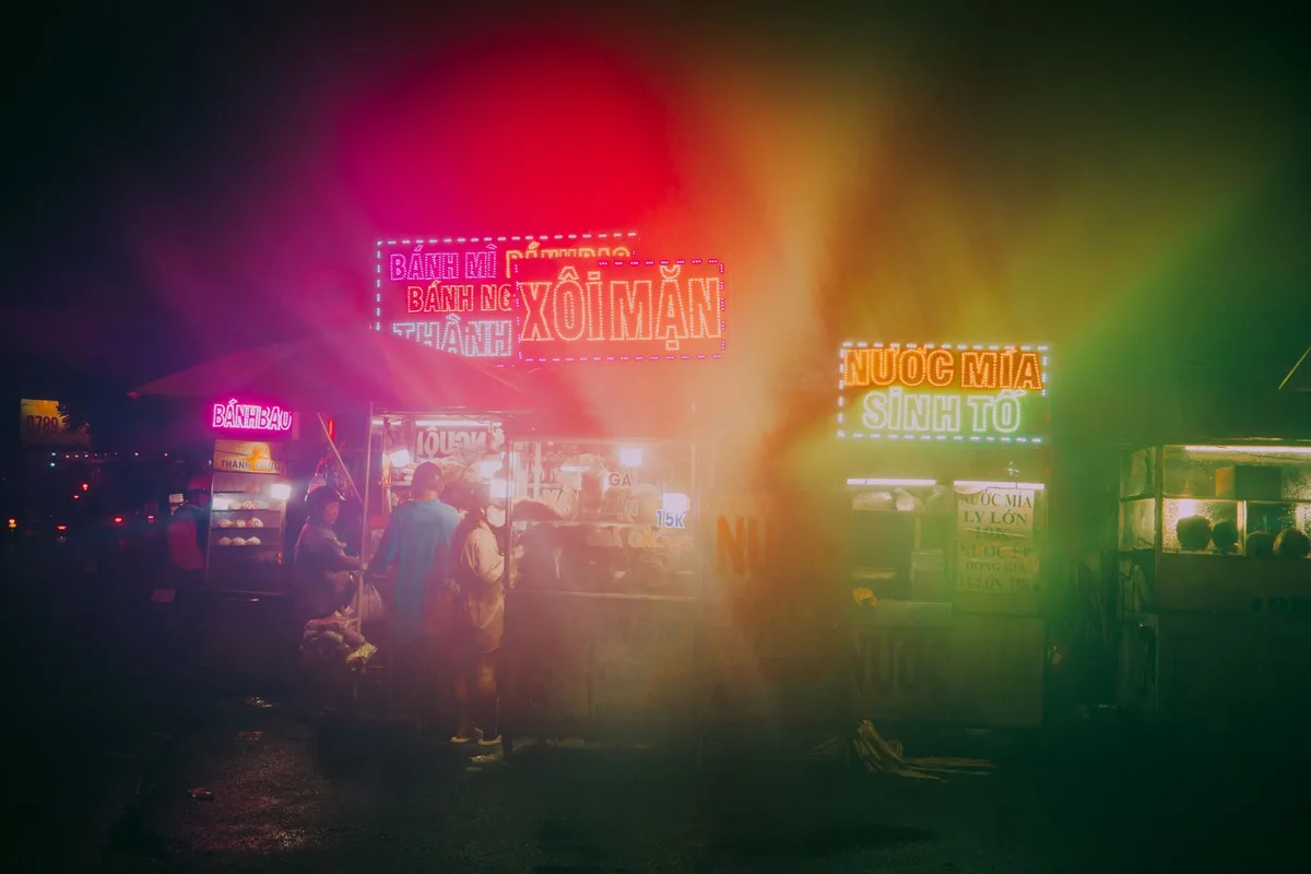 A Vietnamese night market after dark, neon signs over the food stalls