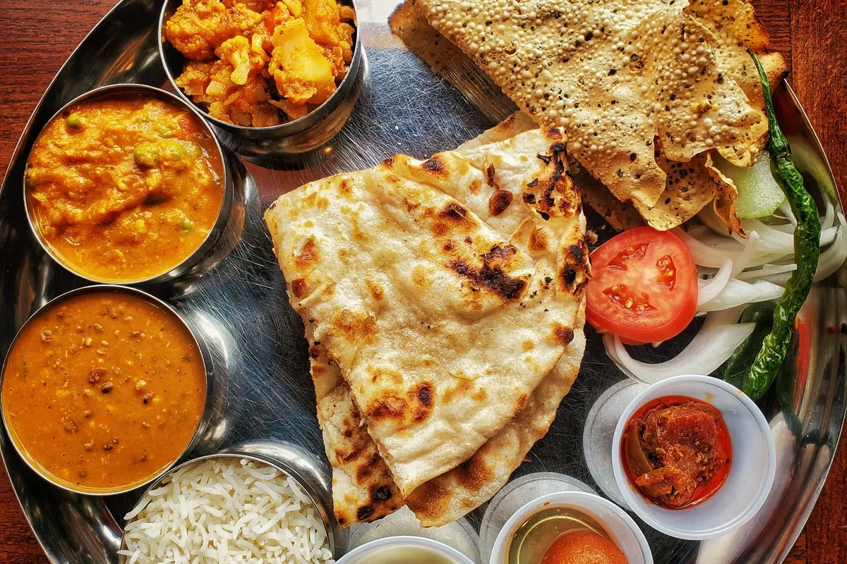 A steel thali of curries, rice, breads and chutneys seen from above