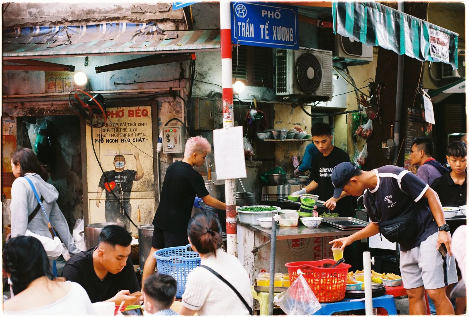 A phở stall on an Old Quarter corner, diners on plastic stools
