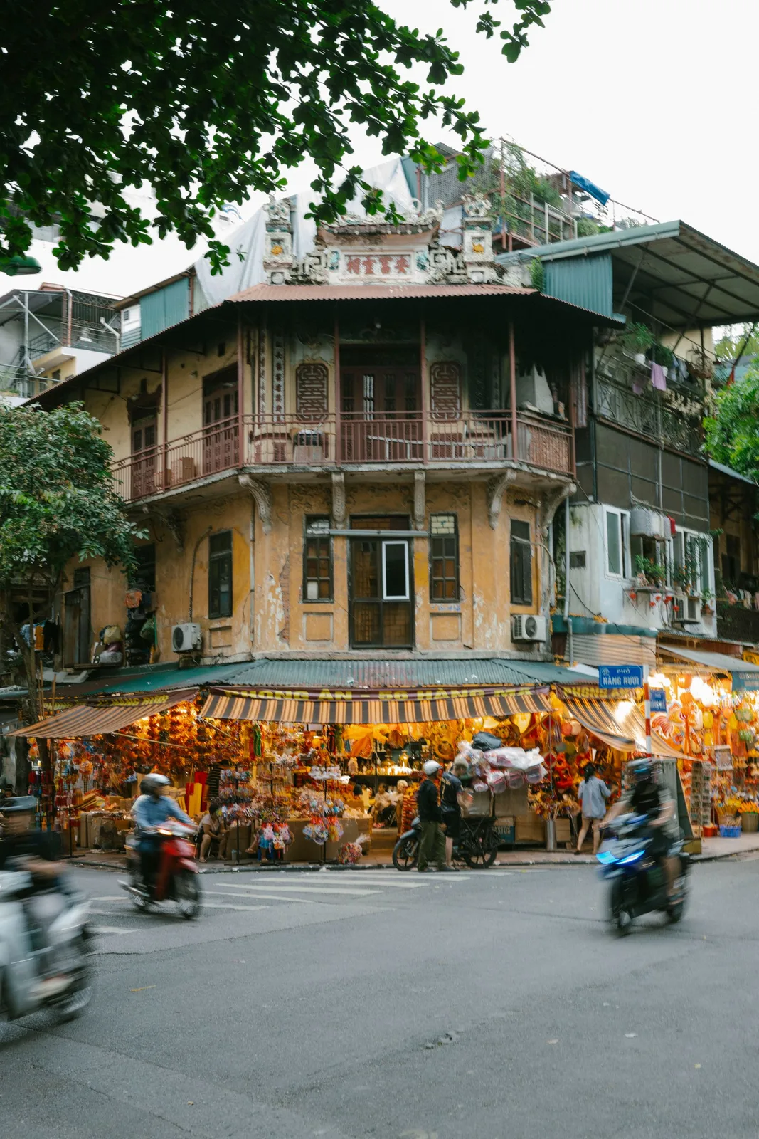 A heritage shophouse corner above festival-goods stalls, scooters passing