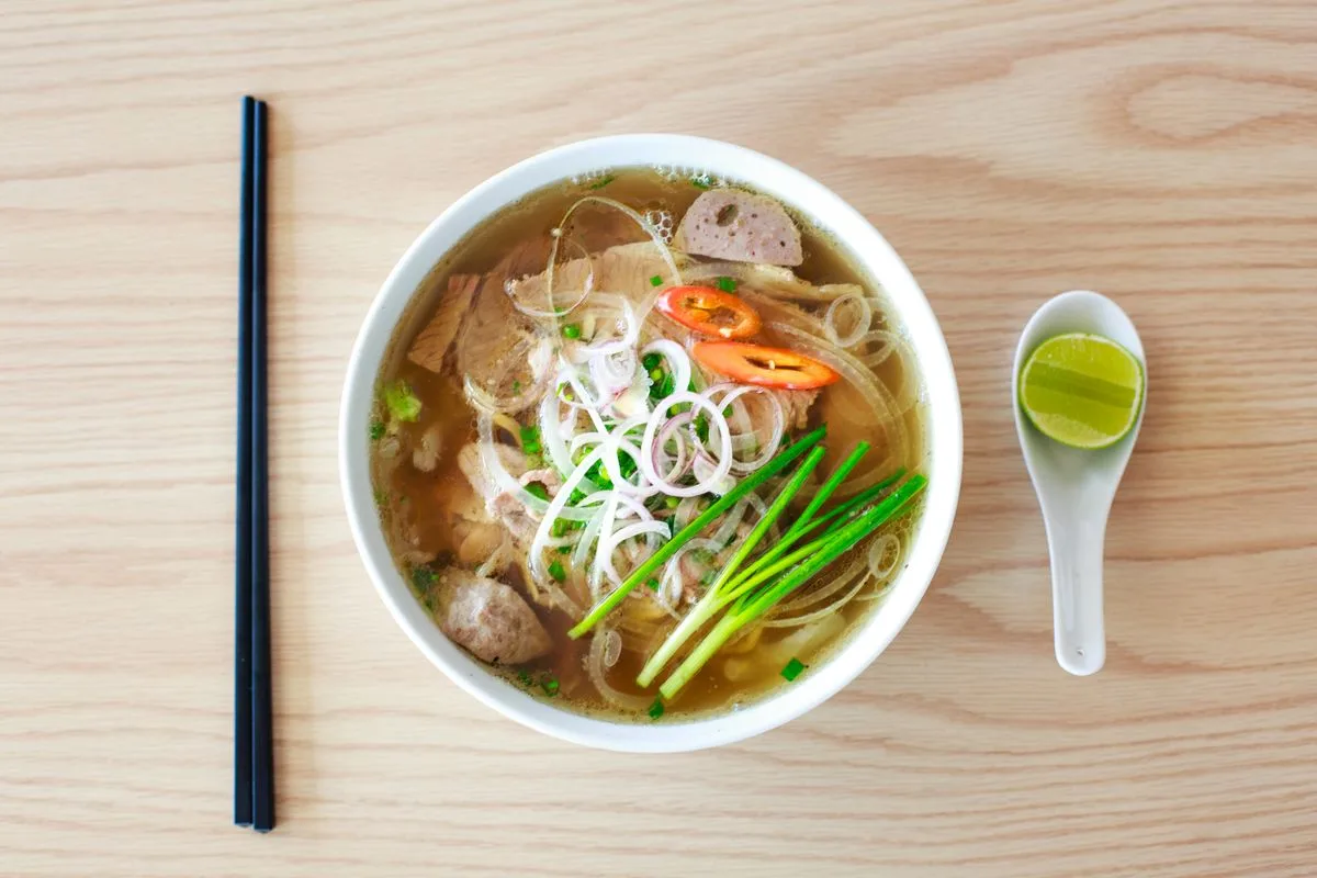 A bowl of pho with beef, herbs, chilli and lime, seen from above