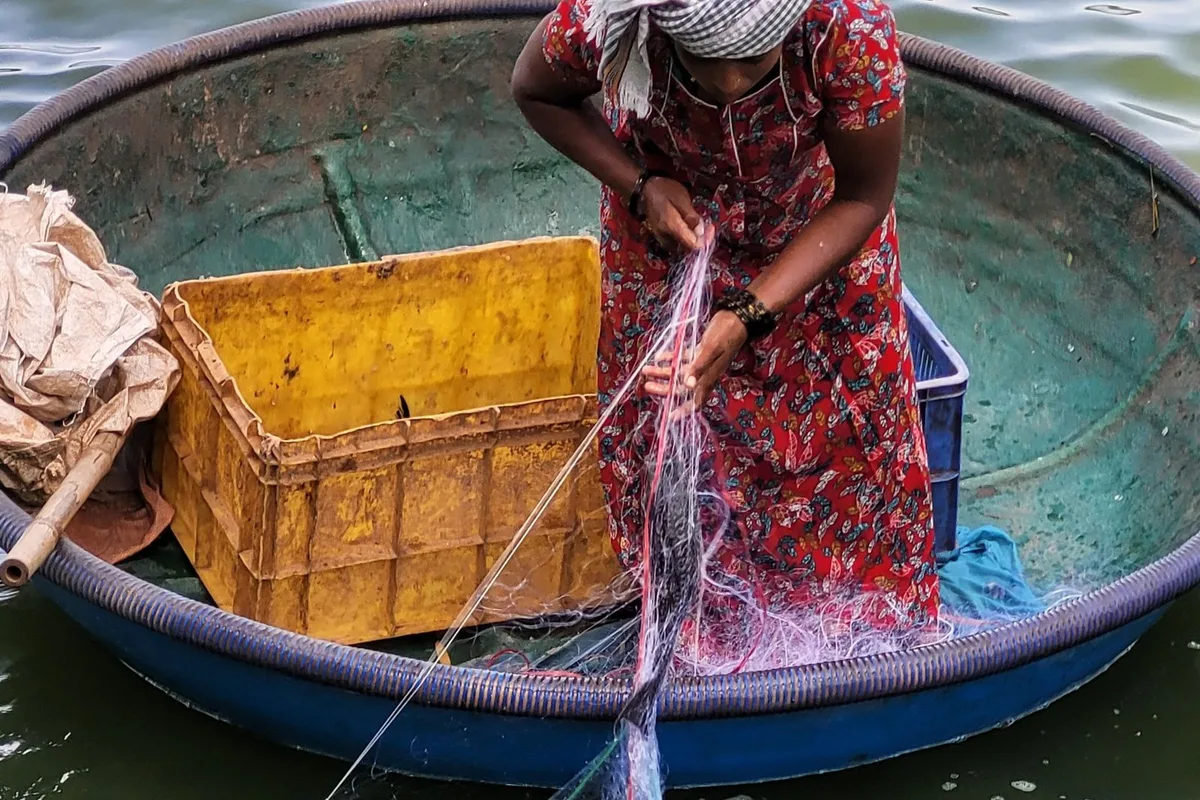 A fisherwoman working from a round basket boat on the river