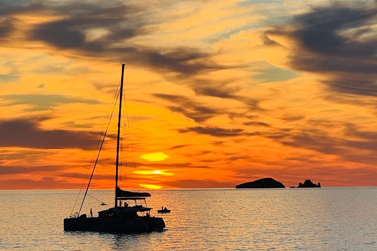 A catamaran silhouetted against an orange sunset at sea off Ibiza