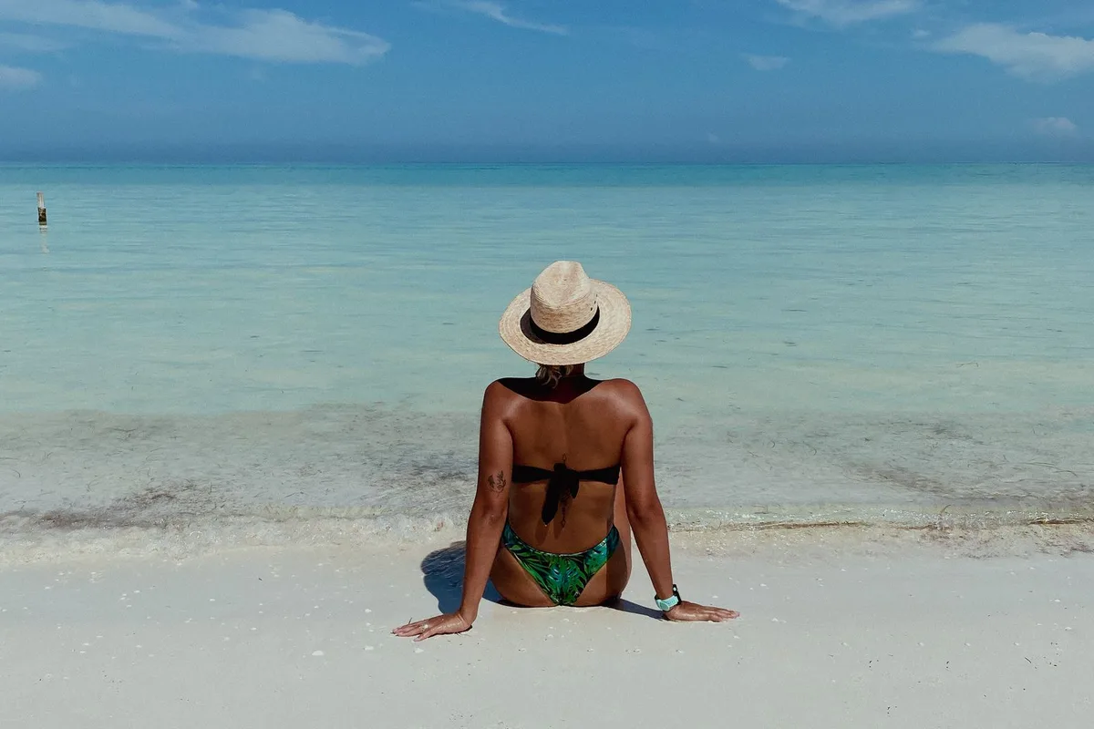 A traveller sitting on the white sand of Isla Holbox facing the turquoise sea