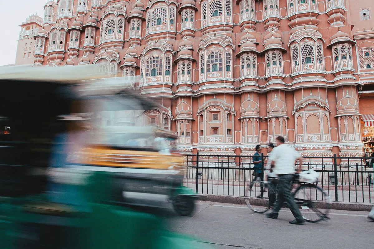 The pink facade of Hawa Mahal in Jaipur as an auto-rickshaw blurs past