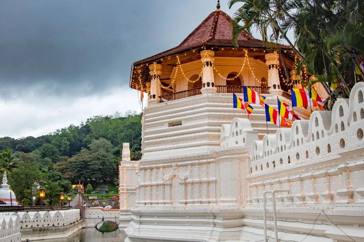 The Temple of the Tooth pavilion across its moat, prayer flags along the white wall