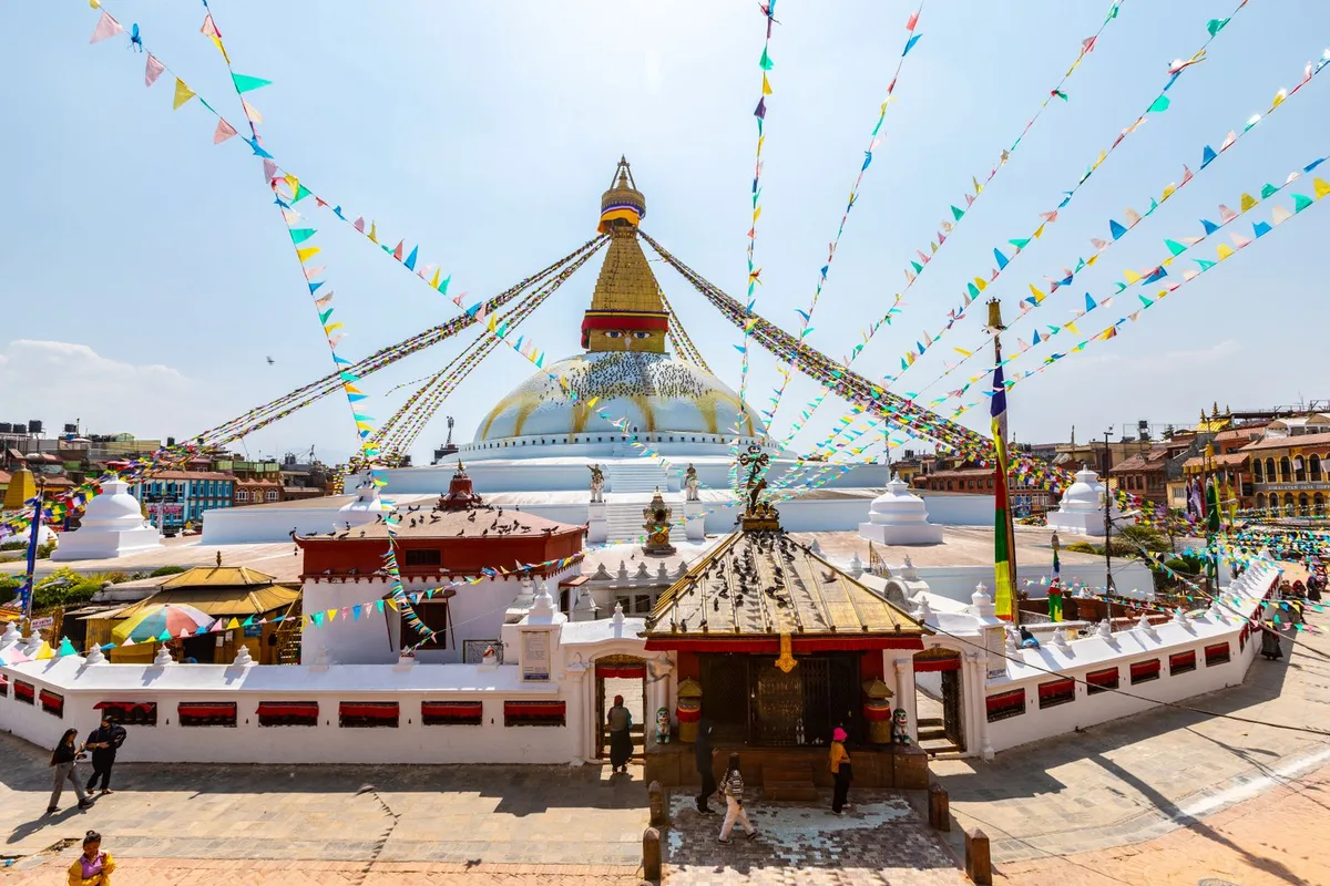 Boudhanath Stupa from above, prayer flags radiating from its gilded spire over the rooftops of Boudha
