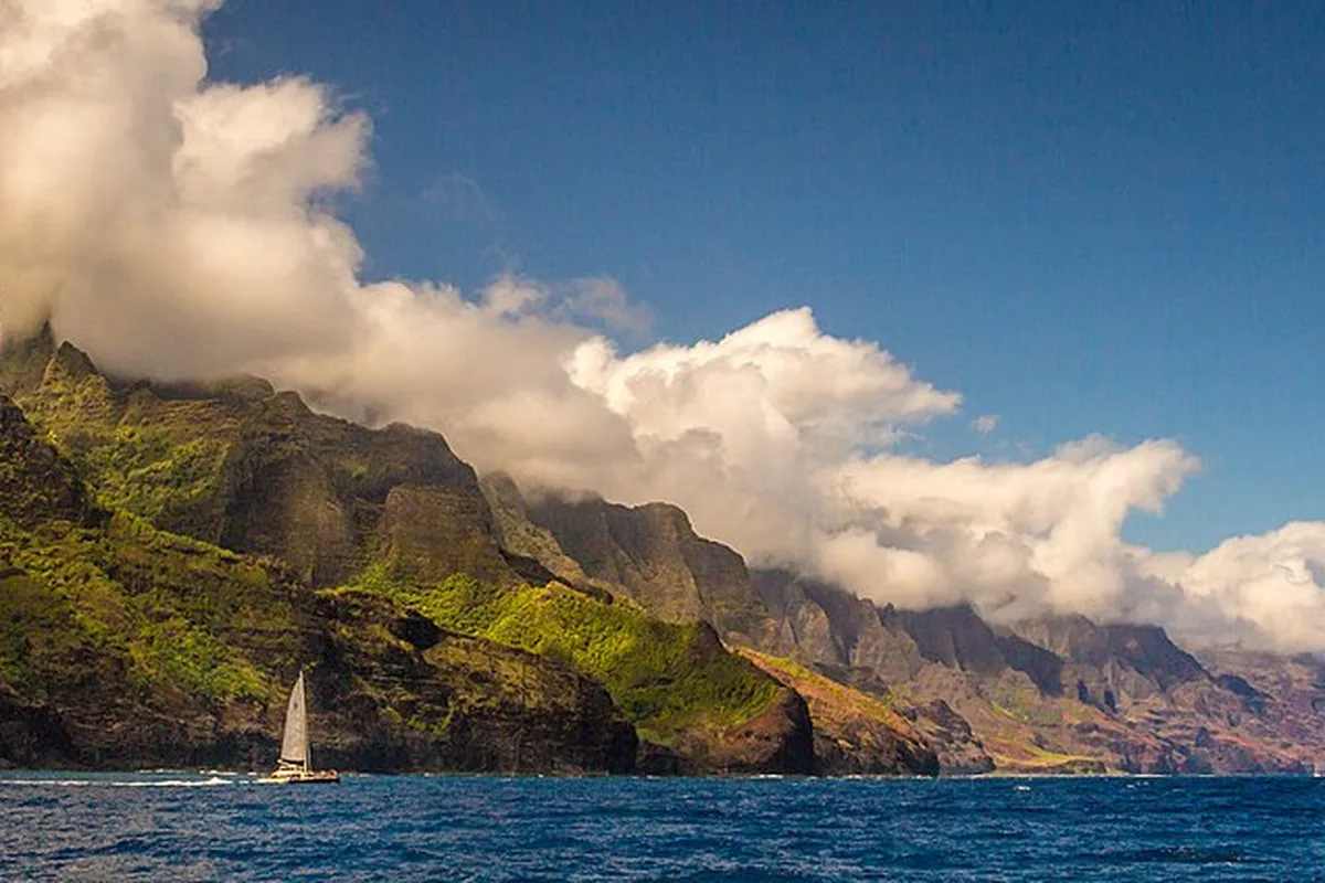 The fluted green cliffs of the Na Pali Coast from the sea, a sailboat below