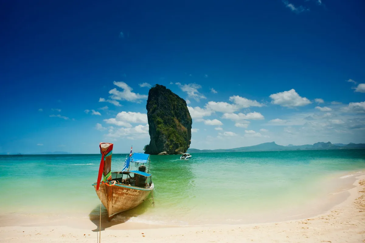 A longtail boat on the white sand of Koh Poda with a limestone stack offshore
