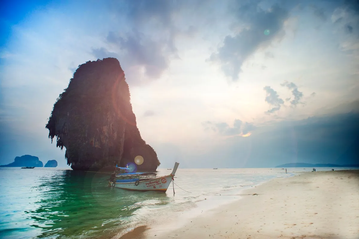A longtail boat at anchor under the limestone stack off Phra Nang Beach at sunset