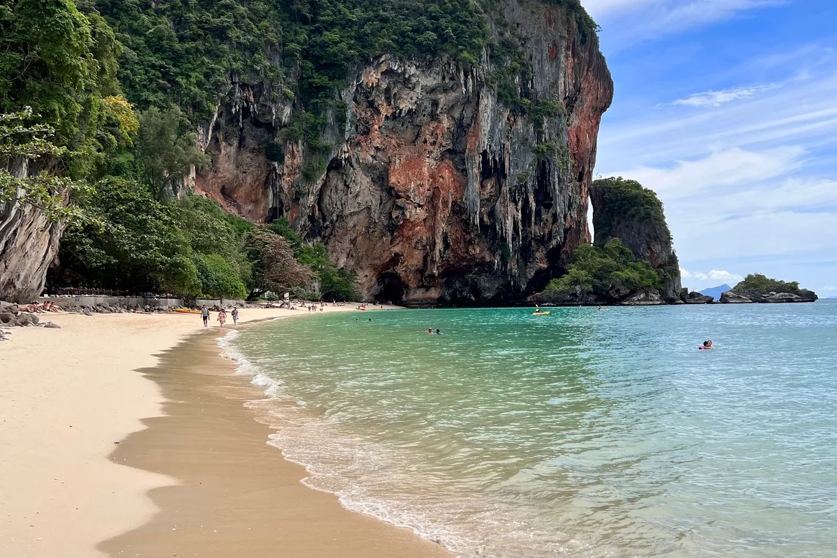 Travellers on the sand beneath the limestone cliffs at Railay Beach