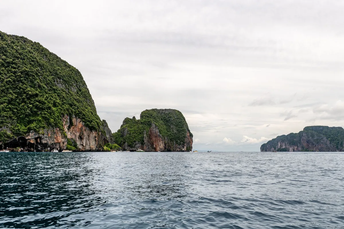 Limestone sea stacks under a grey monsoon sky, seen from a boat